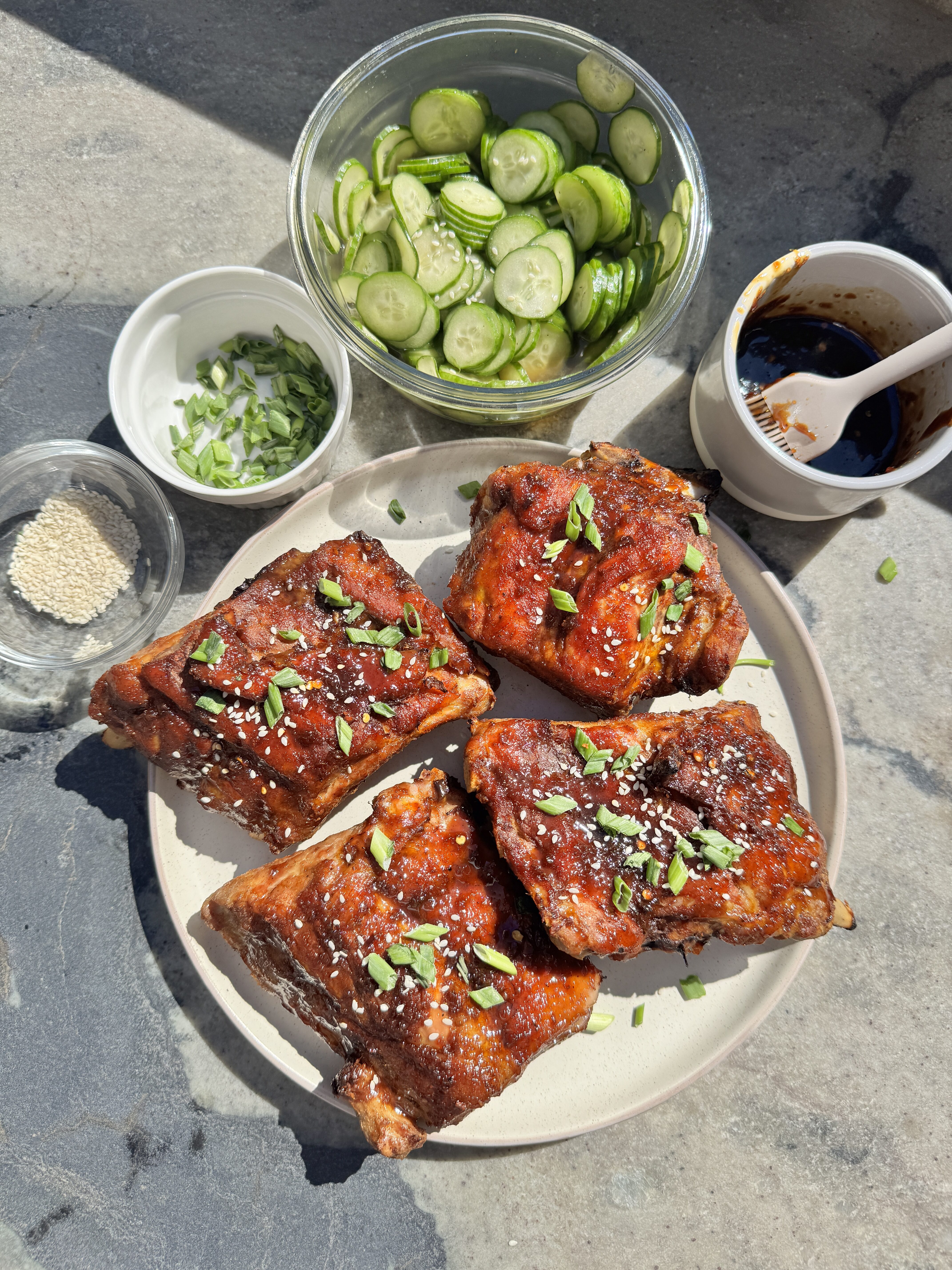 Overhead view of sticky honey garlic Asian ribs on a plate with sliced cucumber salad, sesame seeds and green onion garnish