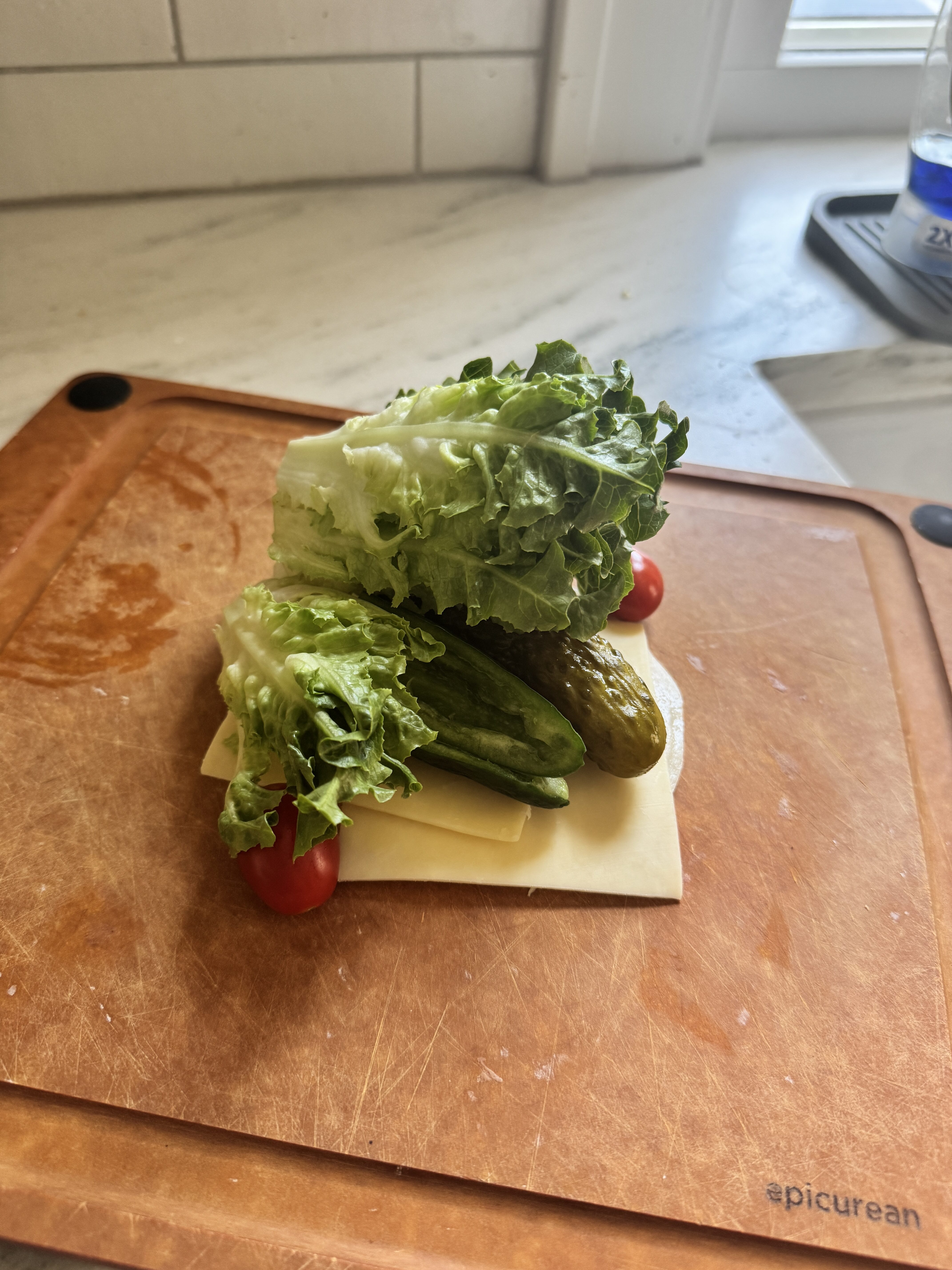 Fresh chopped sub salad ingredients stacked on a cutting board before chopping — lettuce leaves, cheddar cheese slices, pickles, and cherry tomatoes