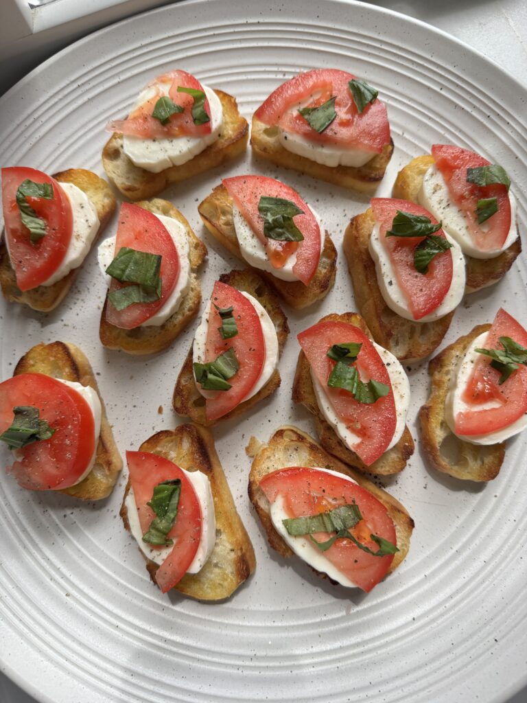 caprese crostini arranged on a platter with basil leaves and balsamic glaze