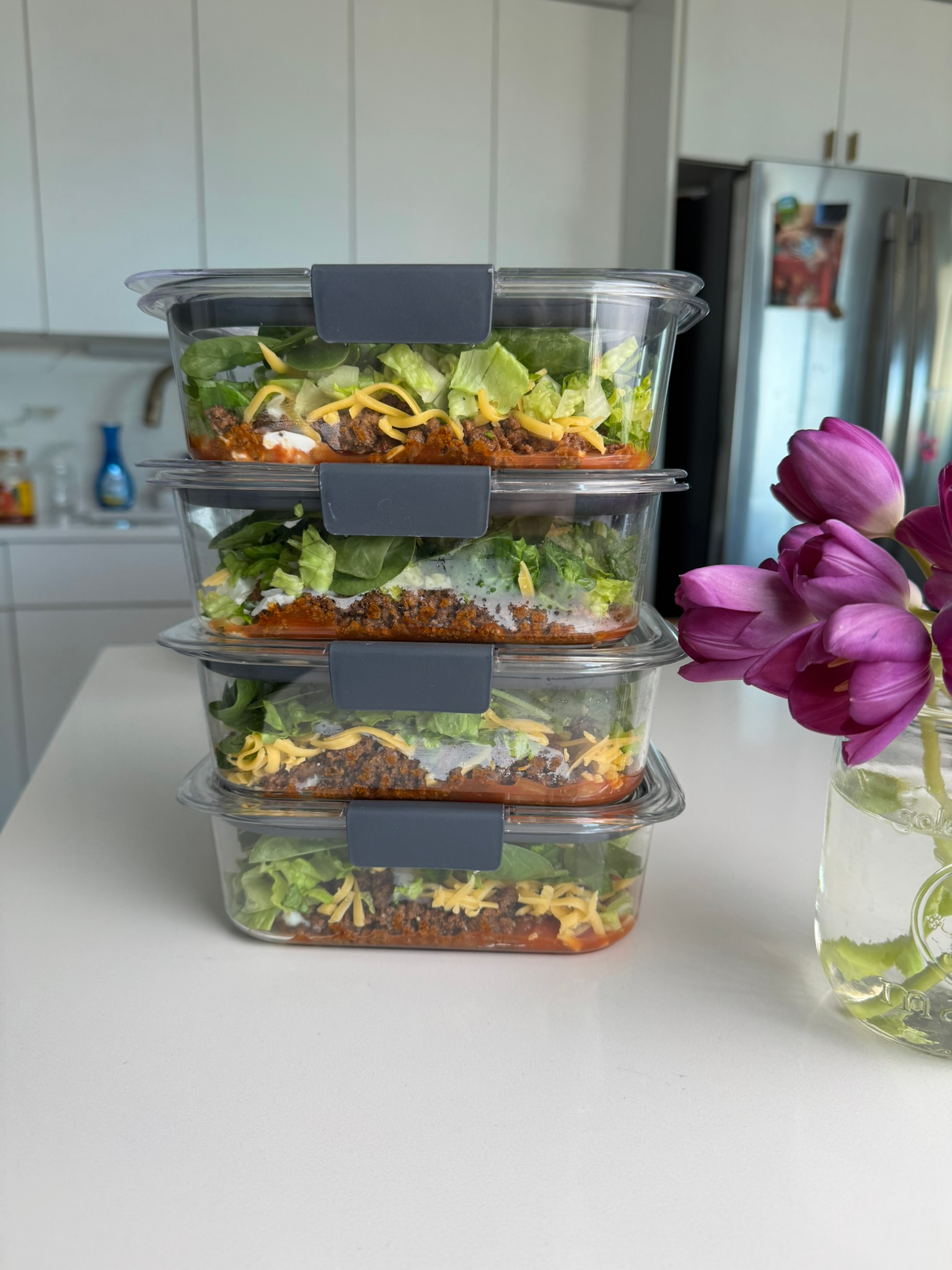 taco salad meal prep containers stacked with lettuce shredded cheese and taco meat