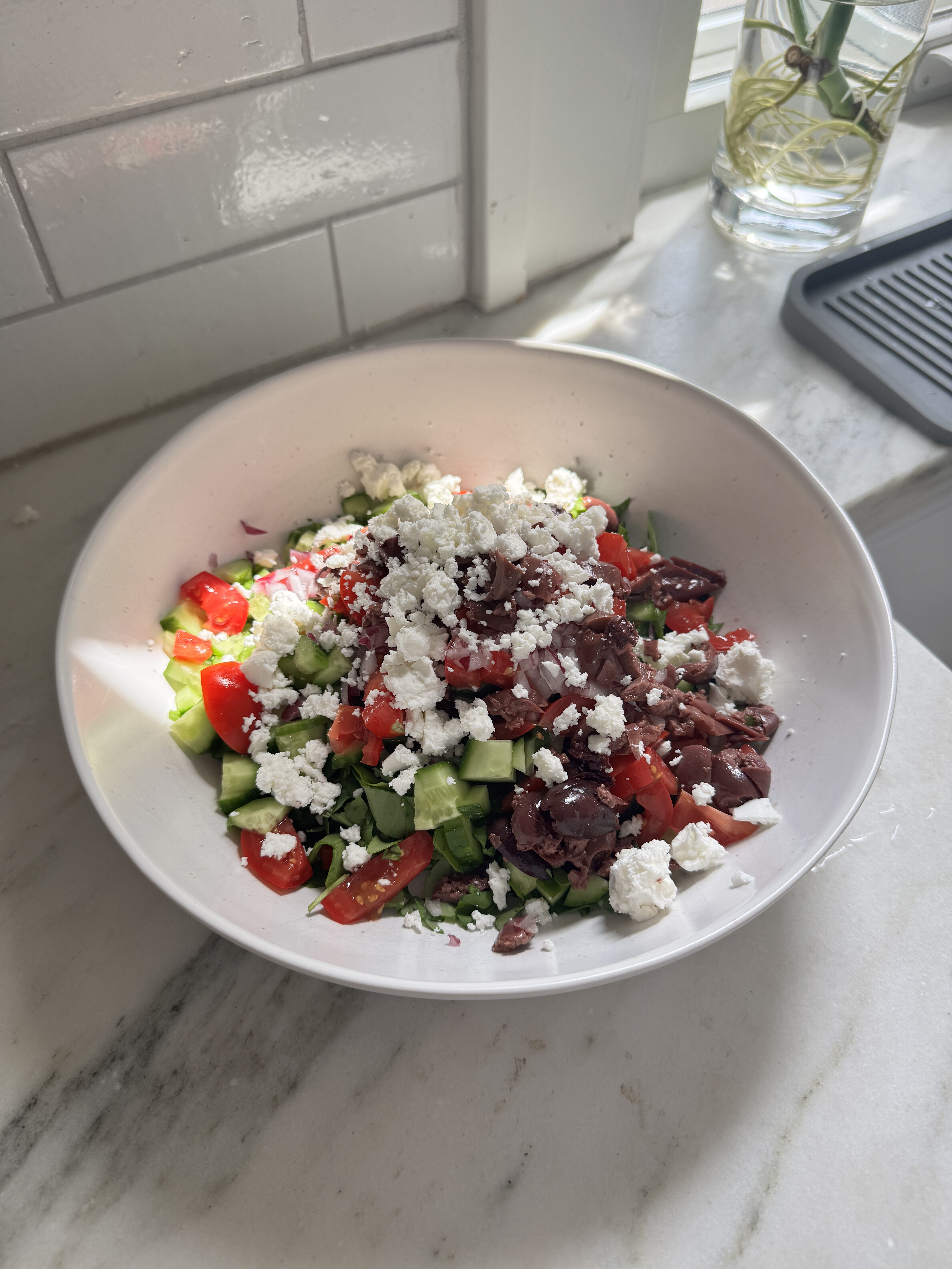 Mediterranean quinoa salad in a white serving bowl topped with feta, kalamata olives, cherry tomatoes, cucumber, and fresh parsley.