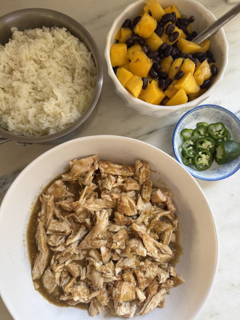 Salsa verde chicken bowl ingredients laid out including shredded chicken, rice, mango, black beans and jalapeno