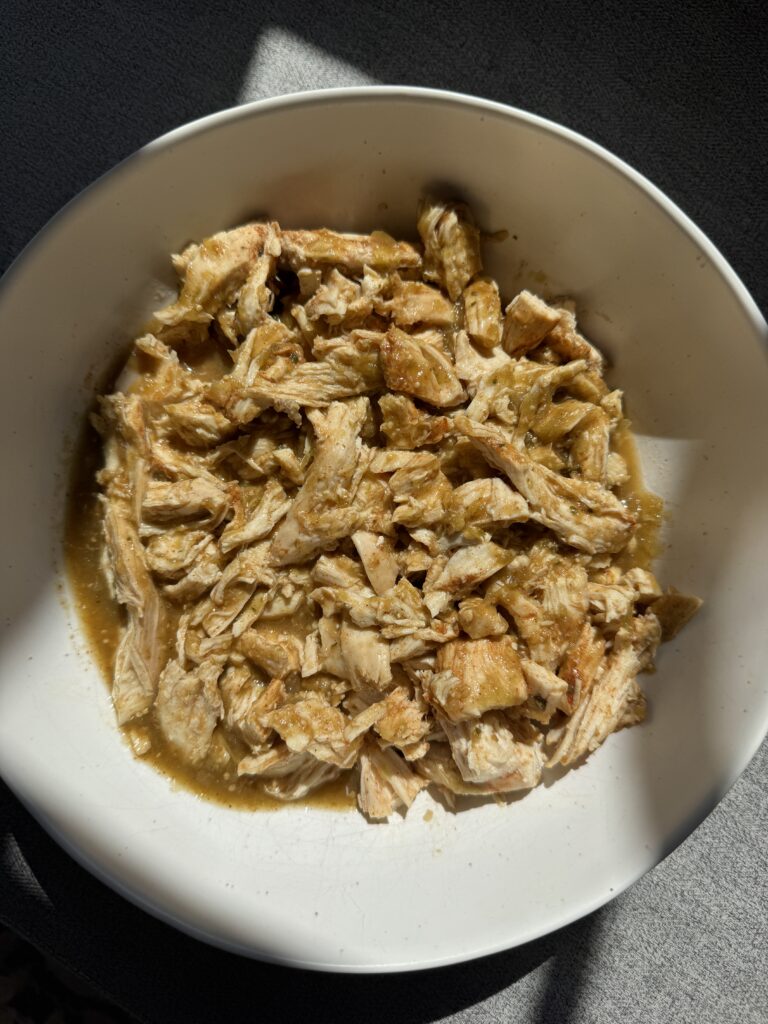Close up of shredded salsa verde chicken in a white bowl ready to assemble into bowls