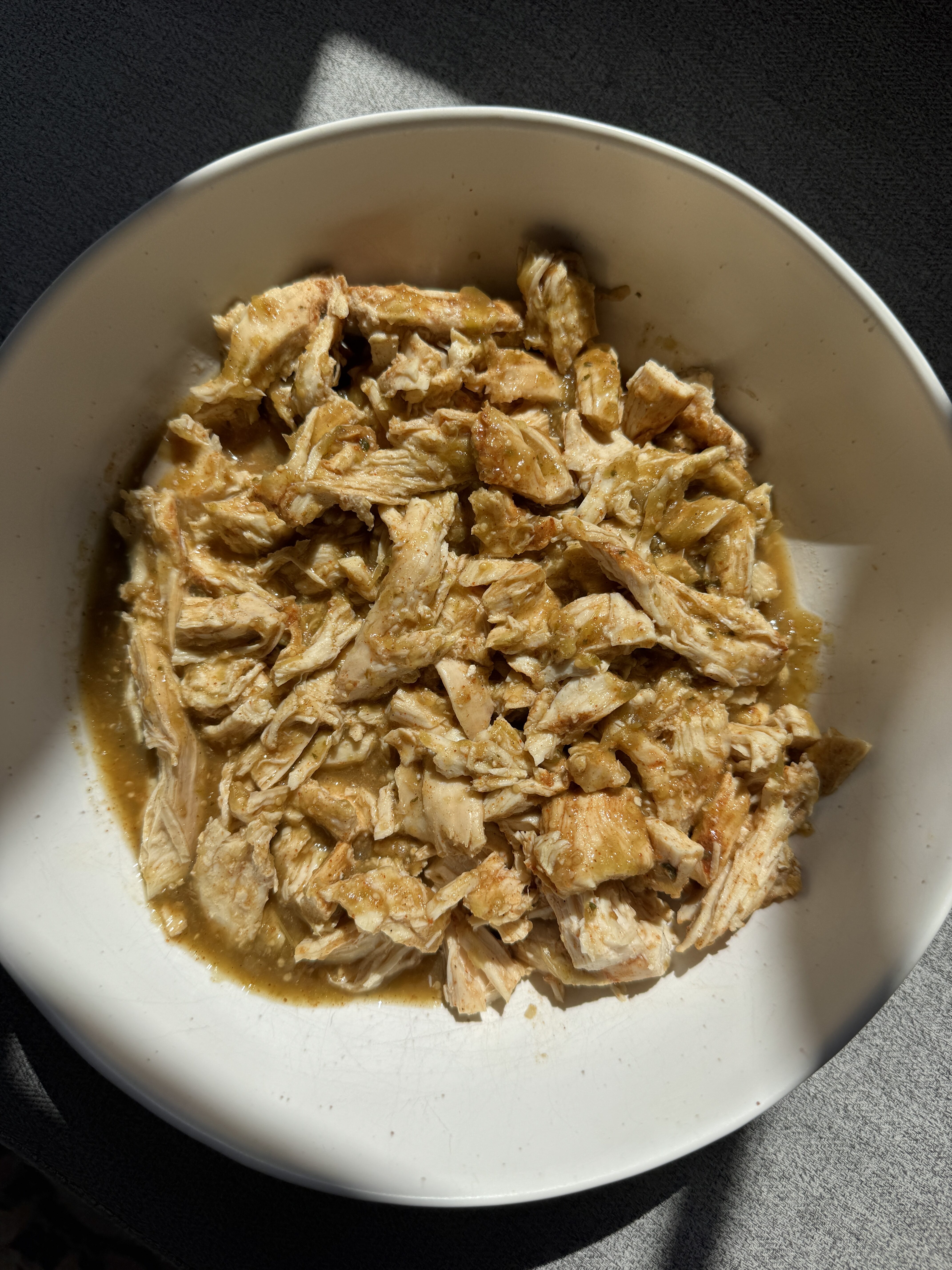 Close up of shredded salsa verde chicken in a white bowl ready to assemble into bowls