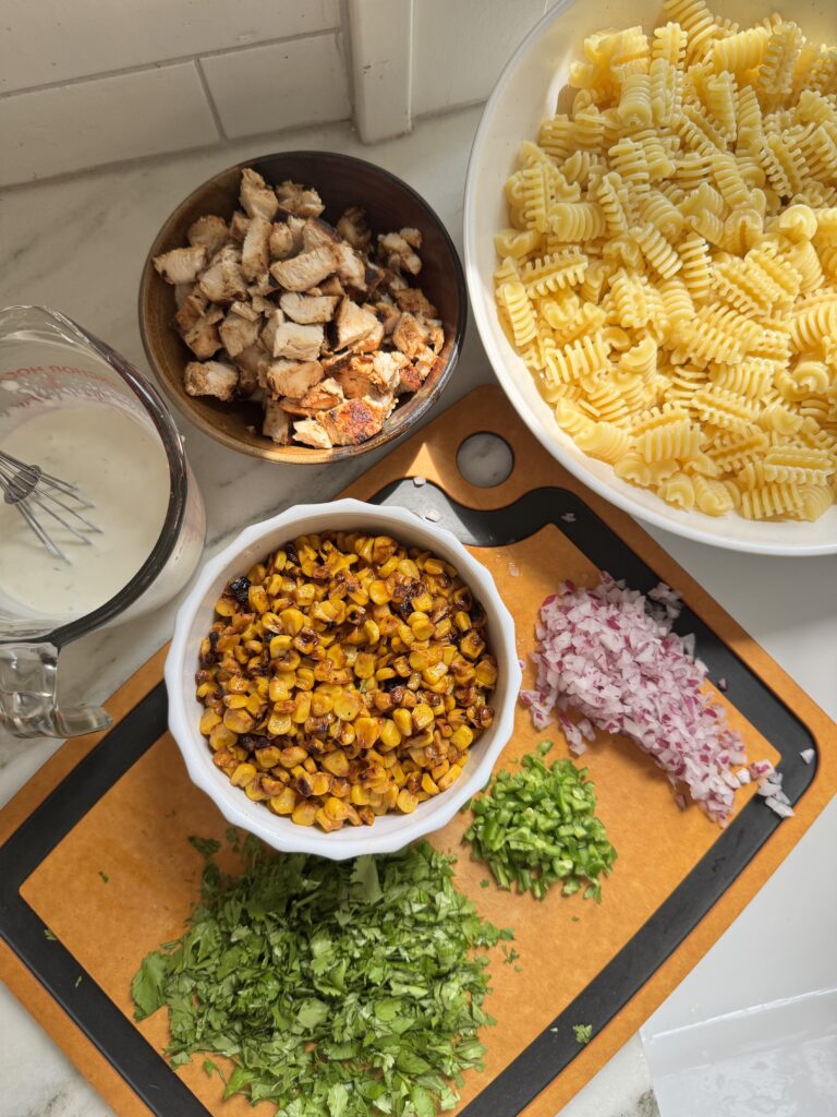 Ingredients for Mexican streetcorn pasta salad with chicken including corn, feta, jalapeños and cilantro laid out on a counter
