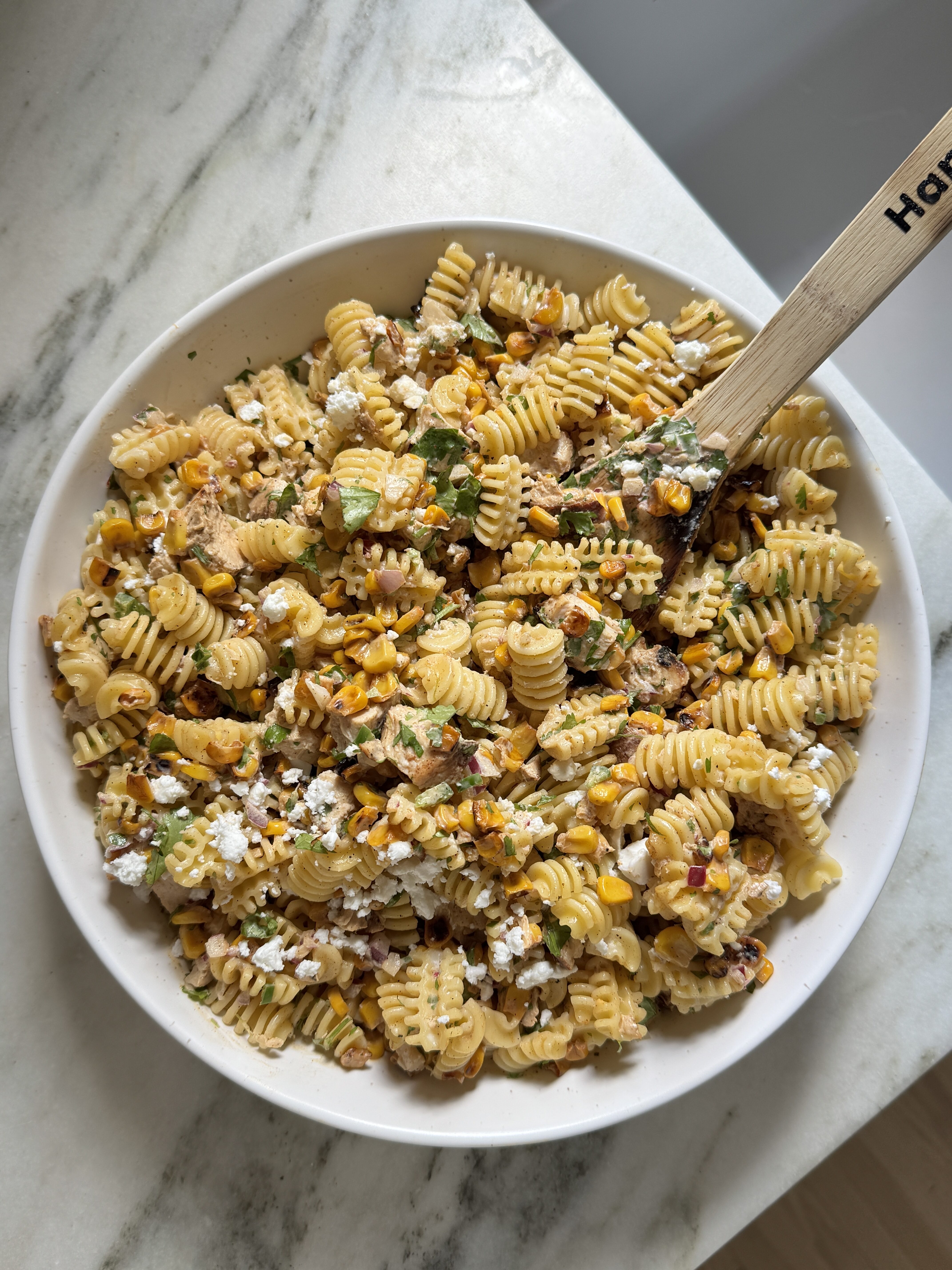 Large white bowl of Mexican streetcorn pasta salad with chicken topped with charred corn, feta cheese and fresh cilantro