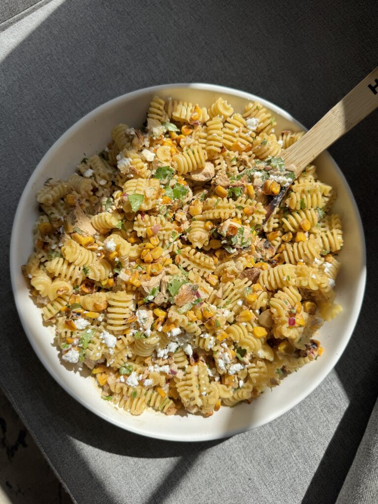 Overhead view of Mexican streetcorn pasta salad with chicken in a white serving bowl with a wooden spoon