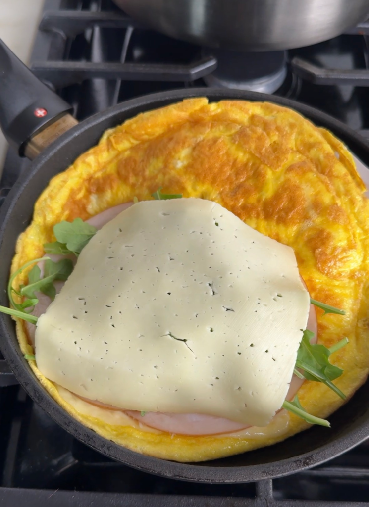 egg tortilla wrap assembly showing havarti cheese, turkey, and arugula layered on the egg in a skillet