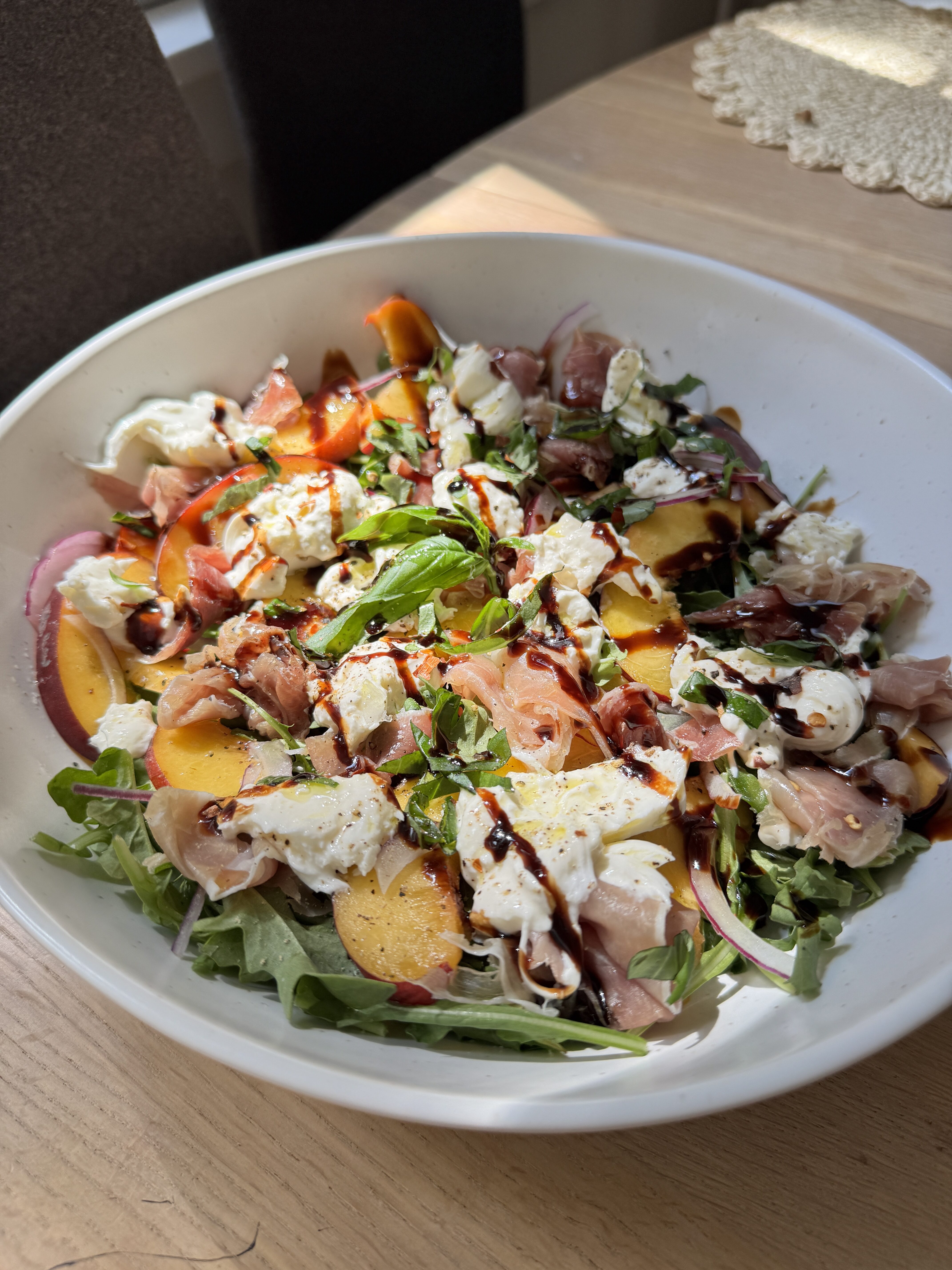 Summer peach burrata salad with arugula, prosciutto, and balsamic glaze on a platter