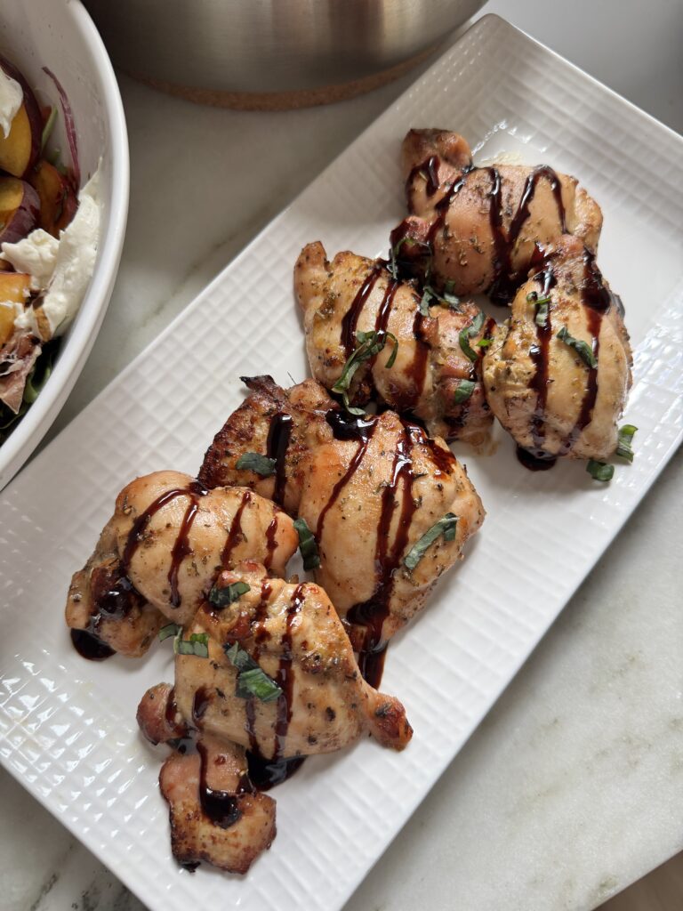 Balsamic chicken thighs on a white platter drizzled with balsamic glaze and topped with fresh basil