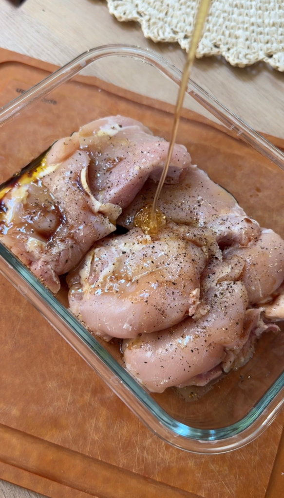 Seasoned chicken thighs in a glass dish being drizzled with honey for balsamic chicken thigh marinade