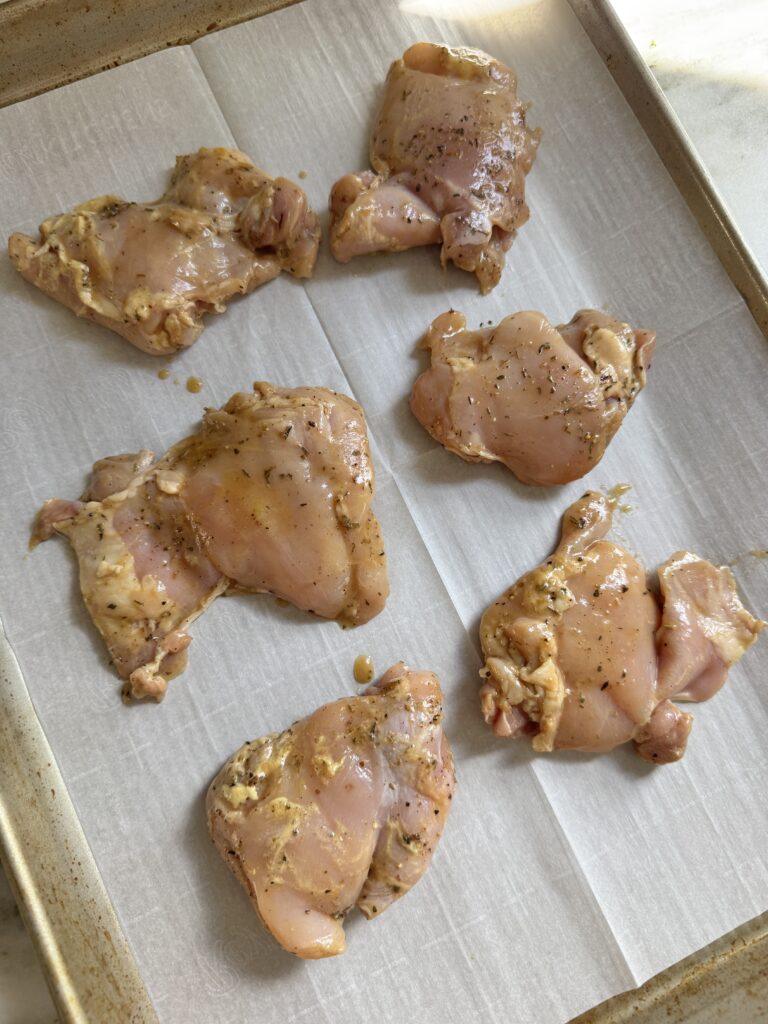 Marinated balsamic chicken thighs arranged on a parchment lined sheet pan before baking
