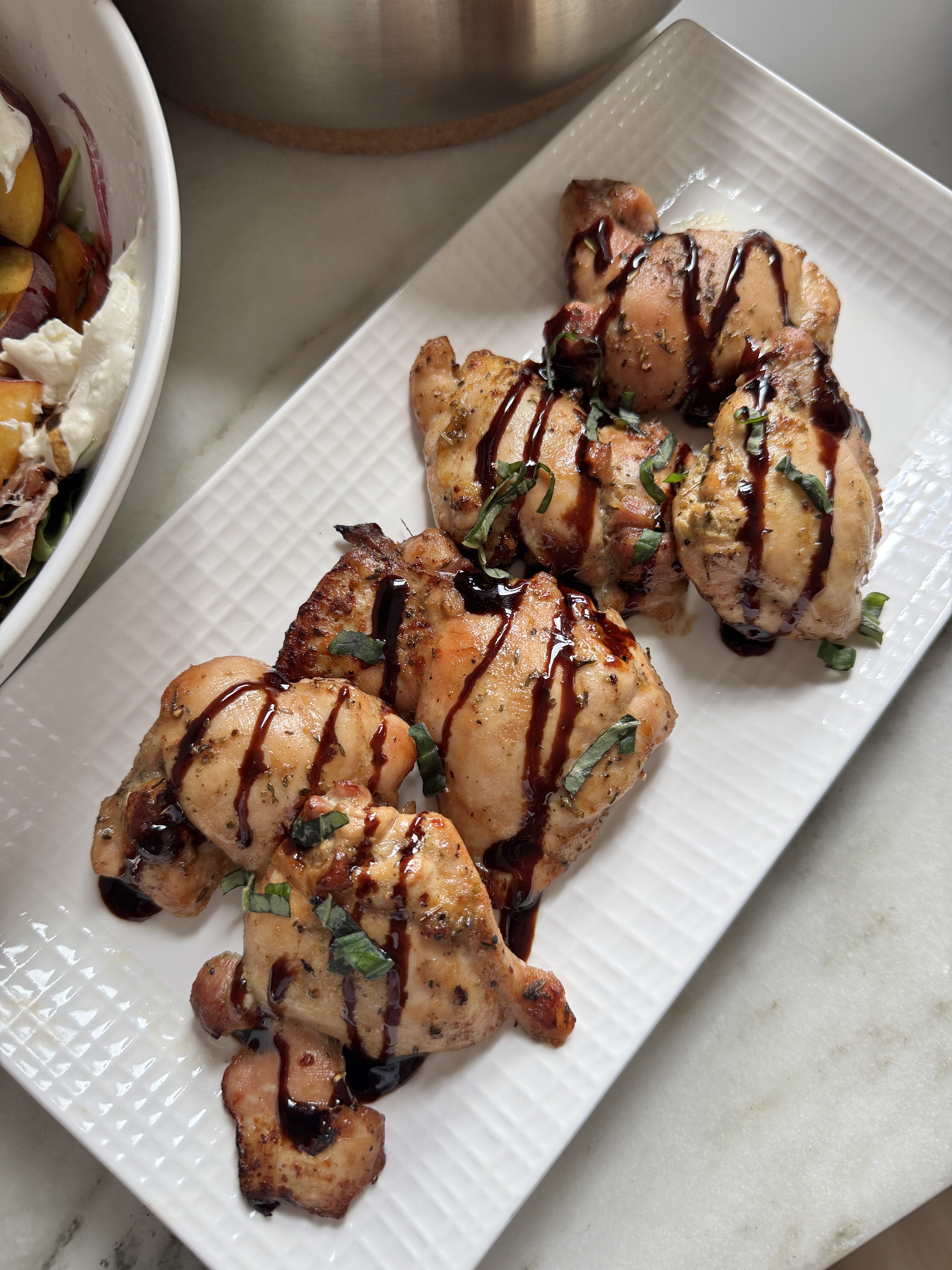 Balsamic chicken thighs on a white platter drizzled with balsamic glaze and topped with fresh basil