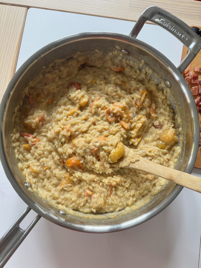 Creamy cherry tomato Boursin orzo stirred together in a pot with a wooden spoon
