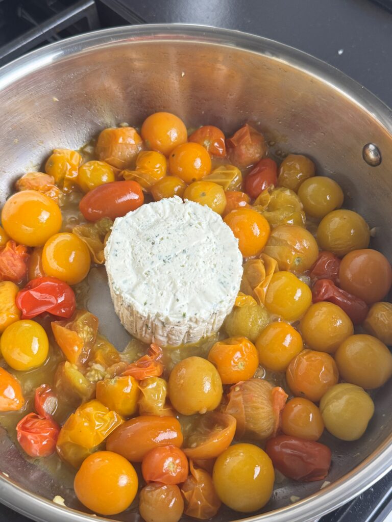 Burst cherry tomatoes around a wheel of herb and garlic Boursin in a skillet