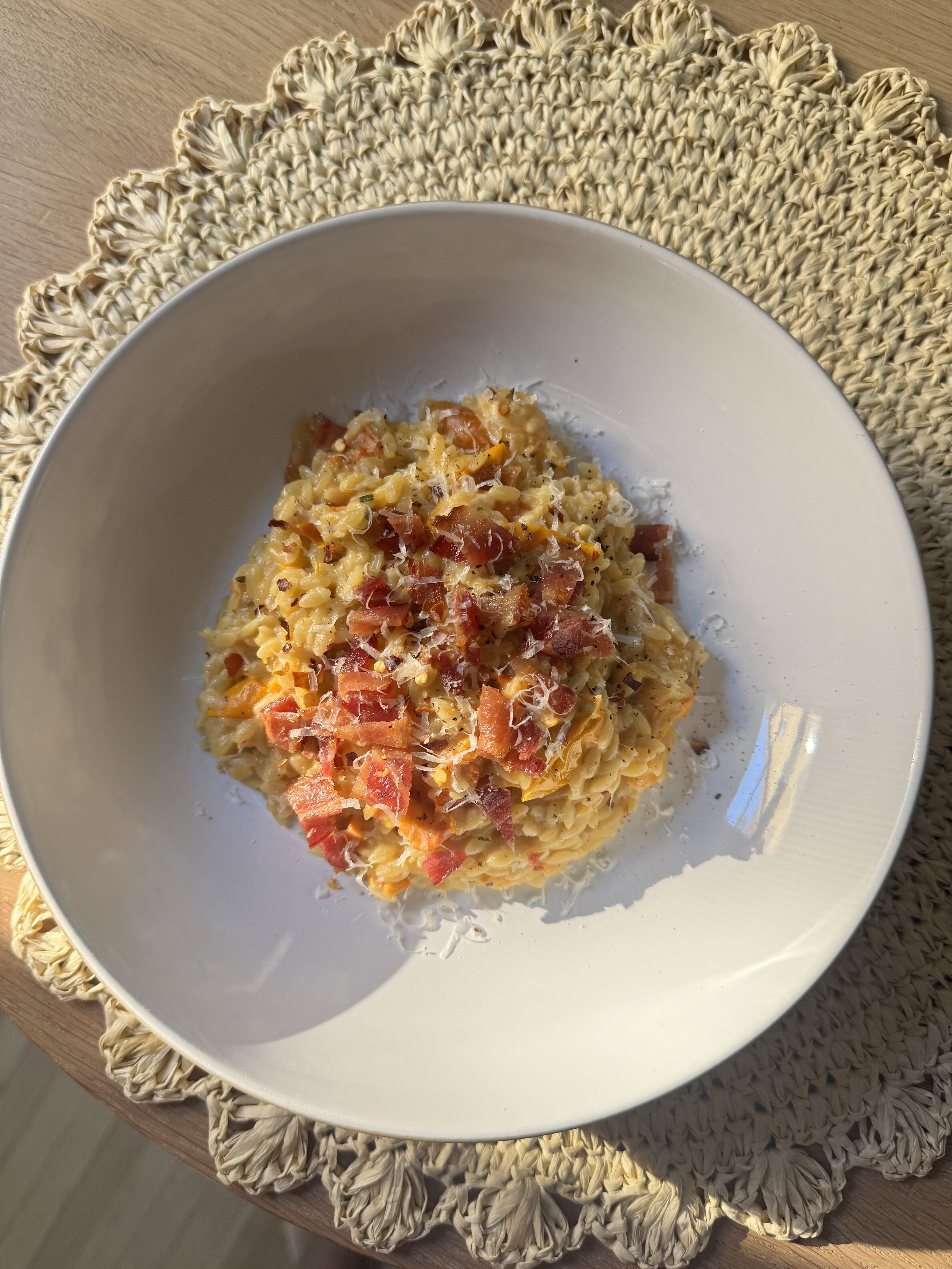 Cherry tomato Boursin orzo in a white bowl topped with crumbled bacon, Parmesan, and chili flakes