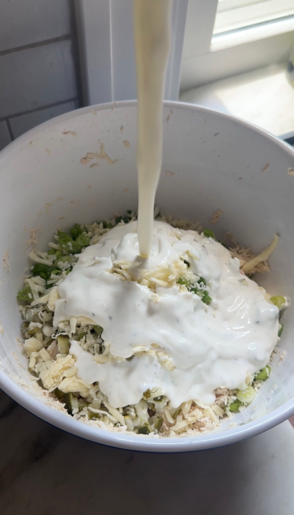 Pouring creamy dill pickle dressing over shredded chicken salad in a bowl