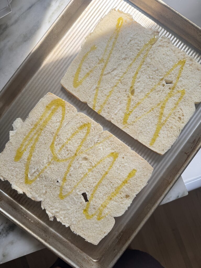 Hawaiian rolls sliced in half and drizzled with olive oil on a baking sheet before toasting