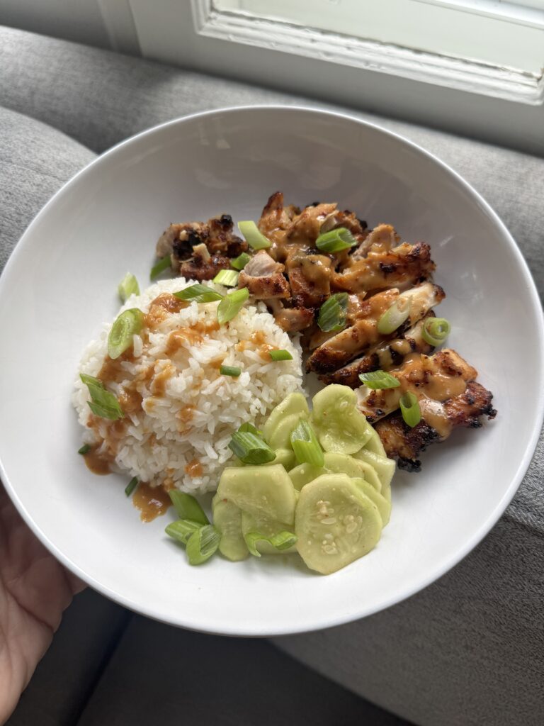 Peanut chicken thighs served over rice with cucumbers and green onion in a bowl