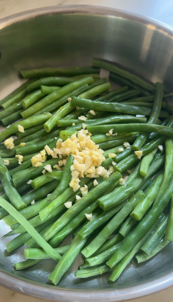 Green beans with minced garlic in a skillet before adding the sesame sauce