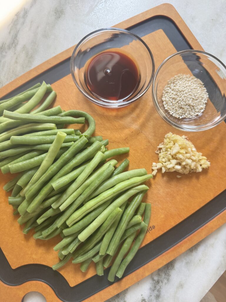 Trimmed green beans, soy sauce, maple syrup, sesame seeds, and minced garlic on a cutting board
