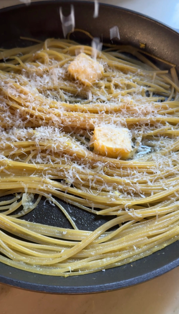 Cooked spaghetti topped with butter and freshly grated Parmesan in a pan for pasta al limone