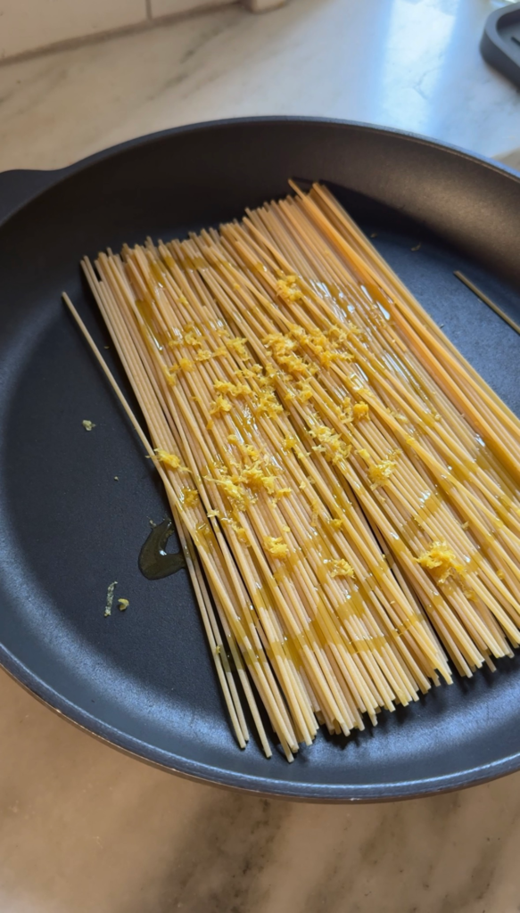 Spaghetti with lemon zest and olive oil in a pan before adding water for one pot pasta al limone