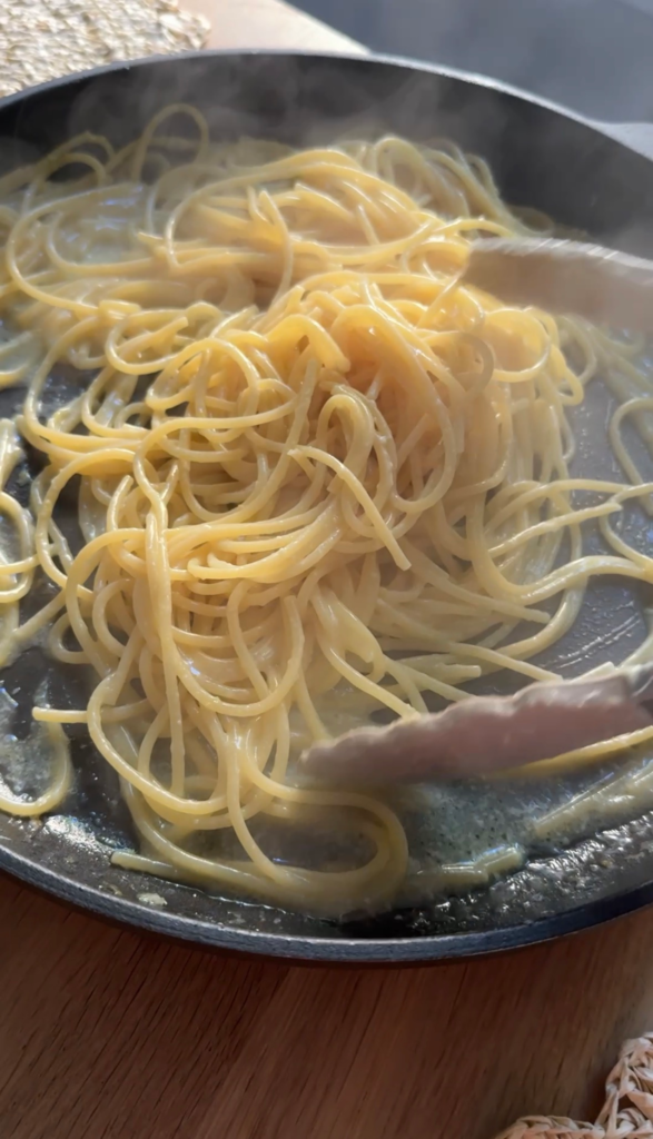 Tossing glossy lemon butter sauce into spaghetti with tongs to finish one pot pasta al limone