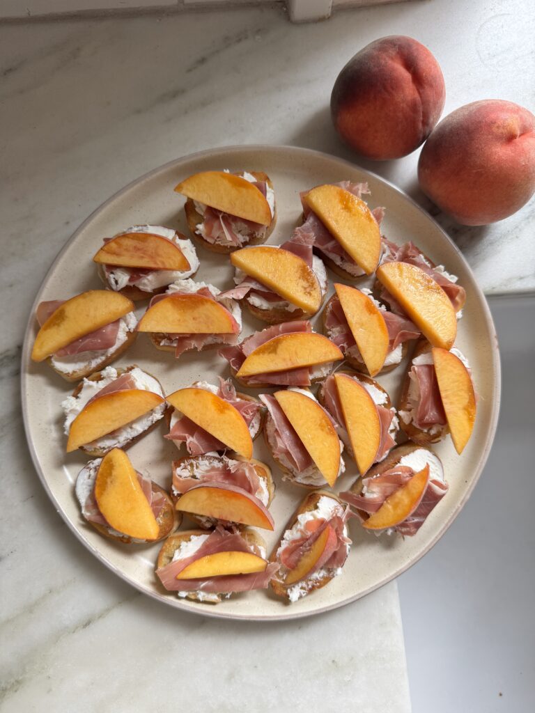 Peach prosciutto crostini on a plate topped with goat cheese, prosciutto, and fresh peach