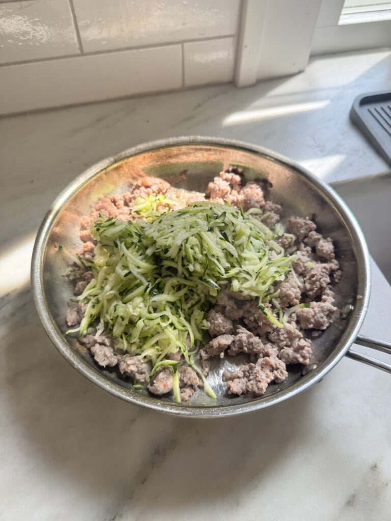 Browned breakfast sausage and shredded zucchini in a skillet