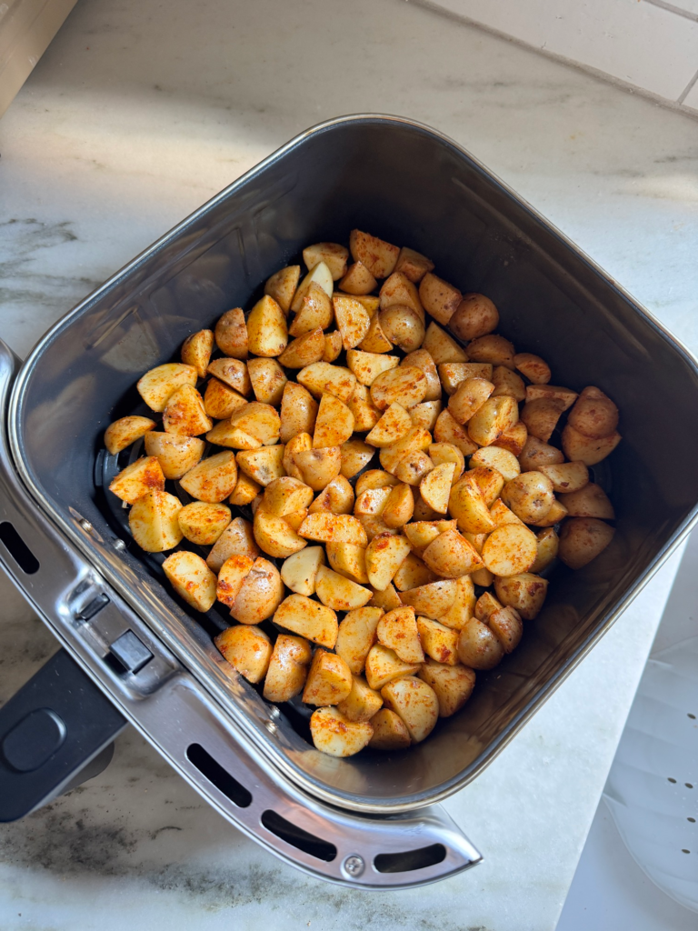 Seasoned potatoes in an air fryer basket before cooking