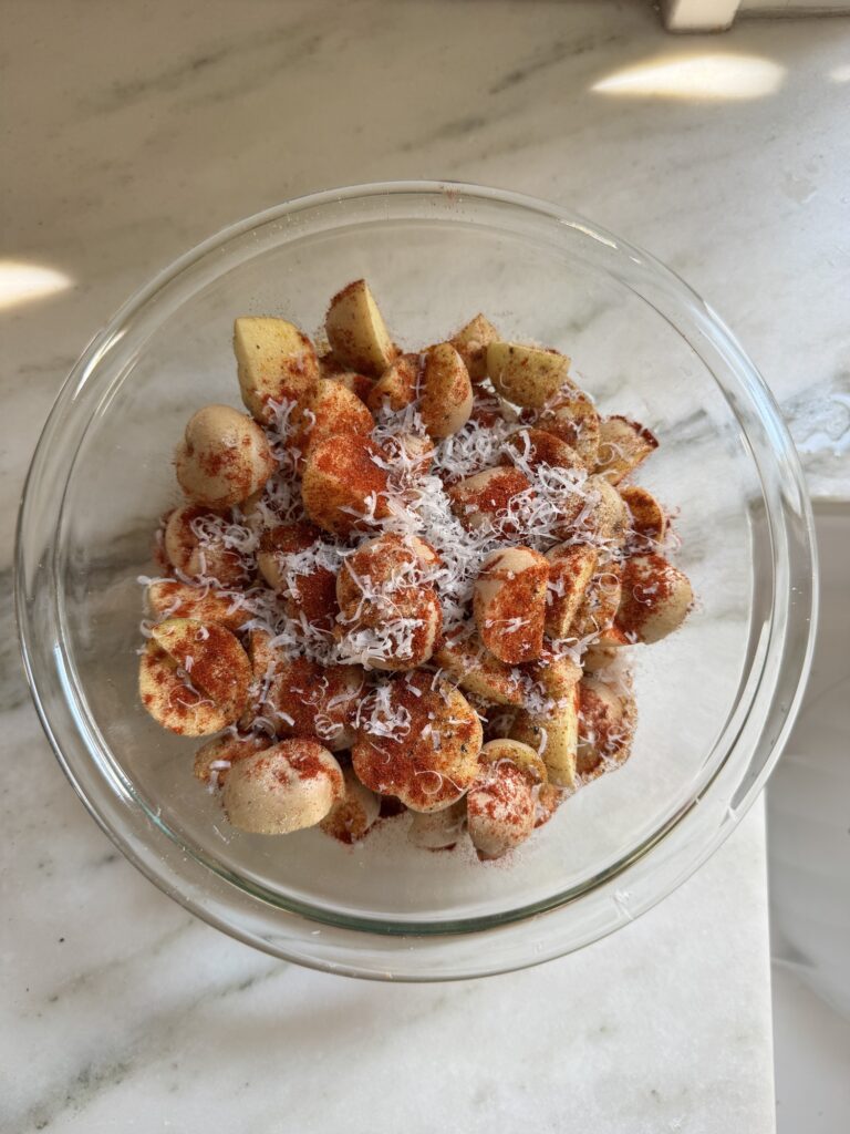 Halved baby potatoes tossed with paprika and Parmesan in a glass bowl