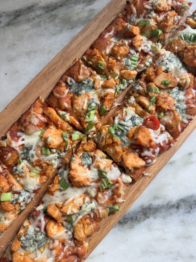 Buffalo chicken flatbread pizza with blue cheese and green onion cut into squares