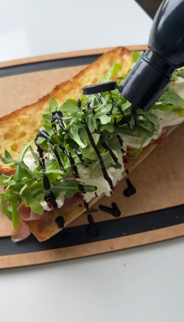 Burrata peach prosciutto sandwich on a baguette topped with arugula and drizzled with balsamic glaze