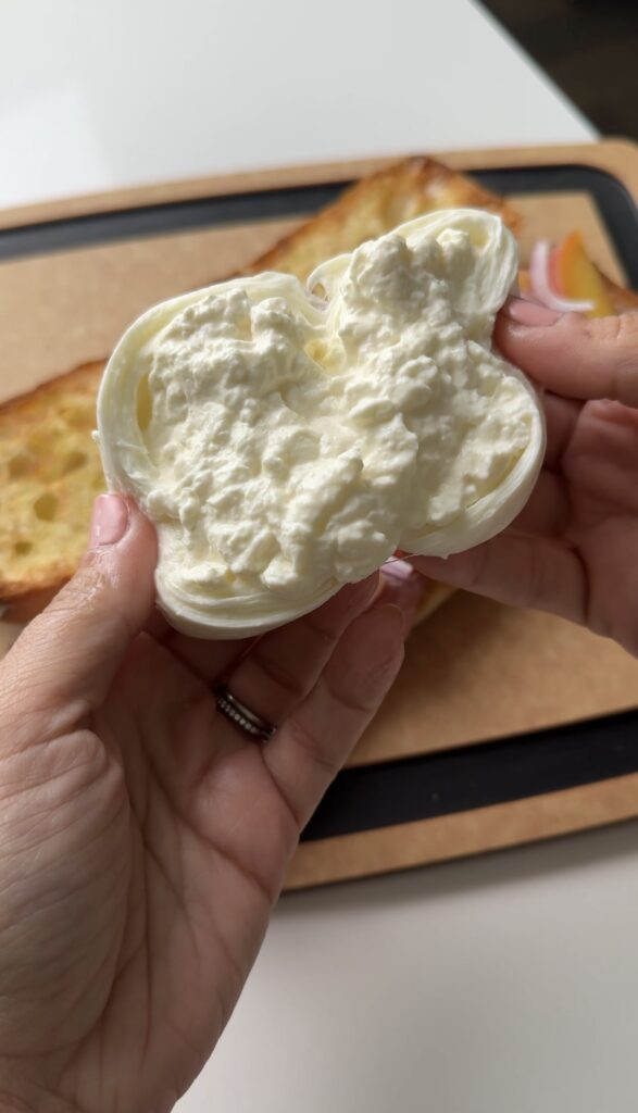 Torn creamy burrata held over a peach prosciutto sandwich