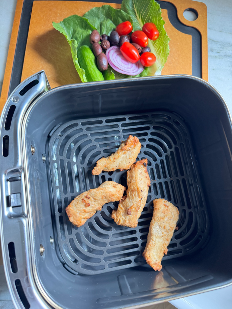 NatureRaised Farms chicken strips in an air fryer basket with veggies on a board