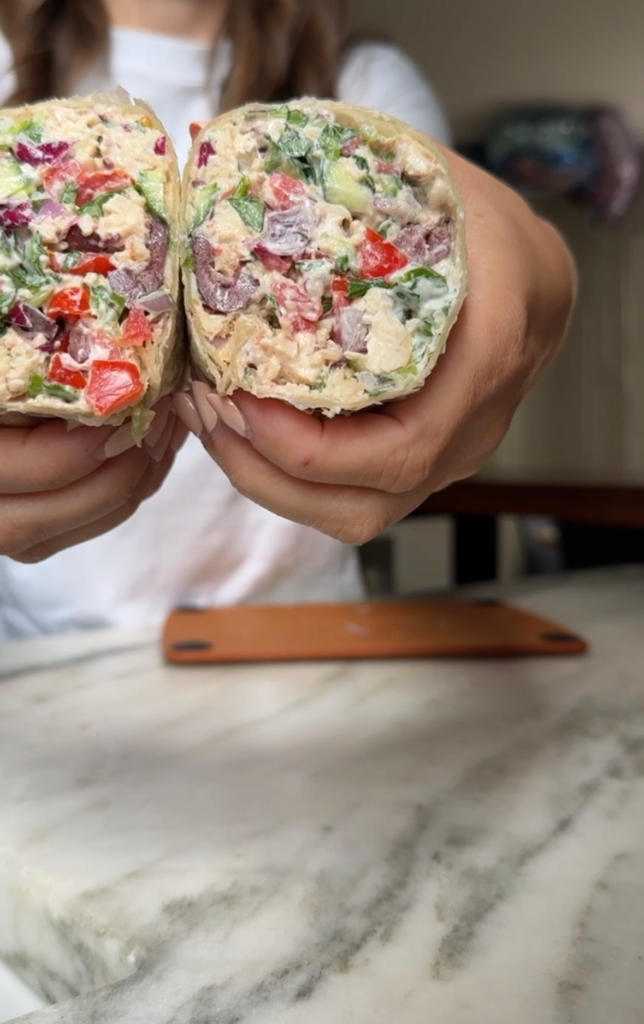 Two halves of a chopped Mediterranean chicken wrap held up to show the filling