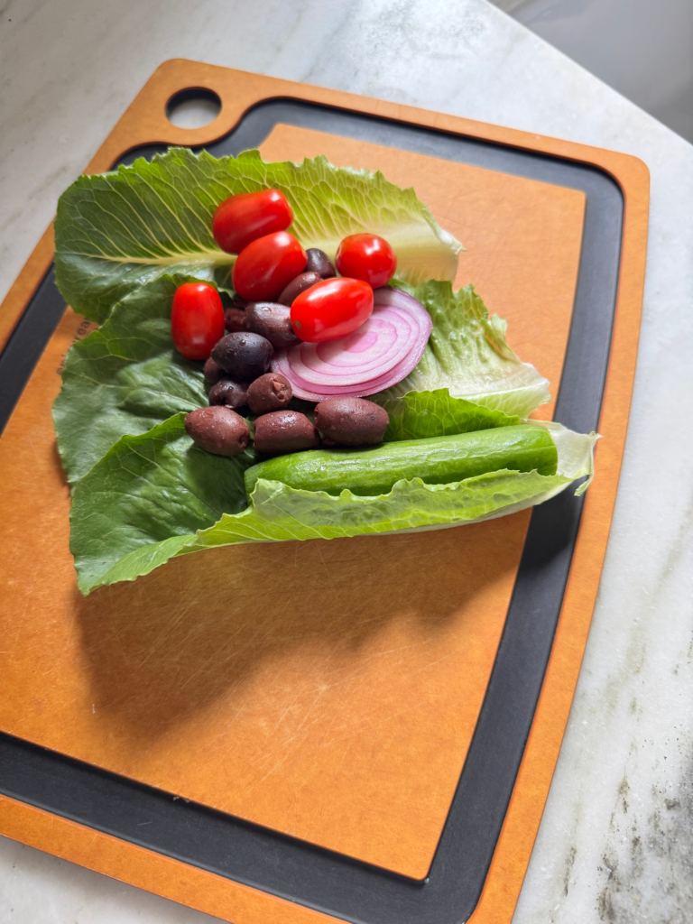 Lettuce, cherry tomatoes, cucumber, red onion, and Kalamata olives on a cutting board
