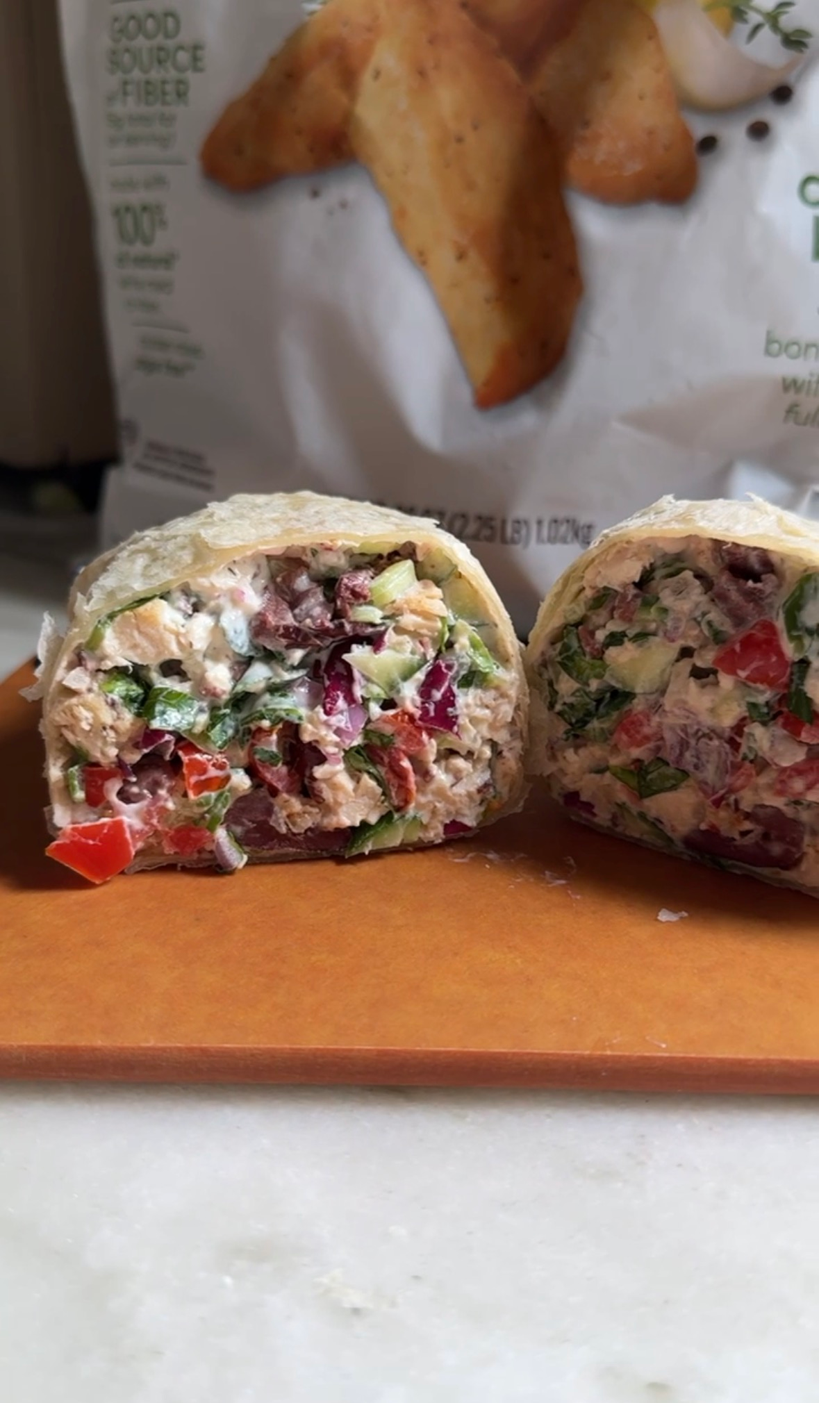 Chopped Mediterranean chicken wrap halves on a board with NatureRaised Farms chicken behind