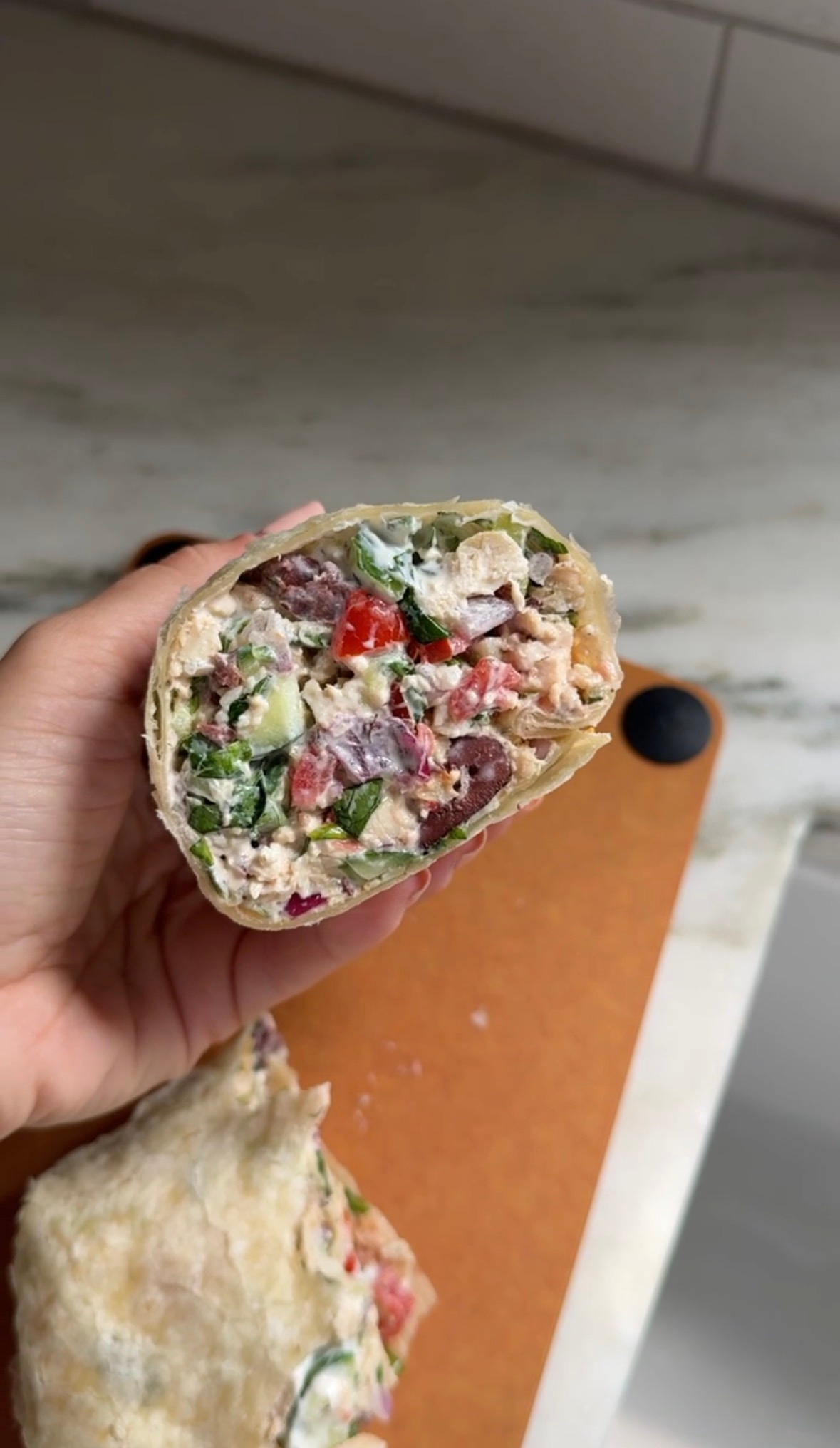 A chopped Mediterranean chicken wrap cut in half showing the chicken, veggies, and tzatziki filling