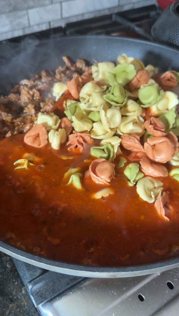 Cheese tortellini added to marinara and sausage in a skillet
