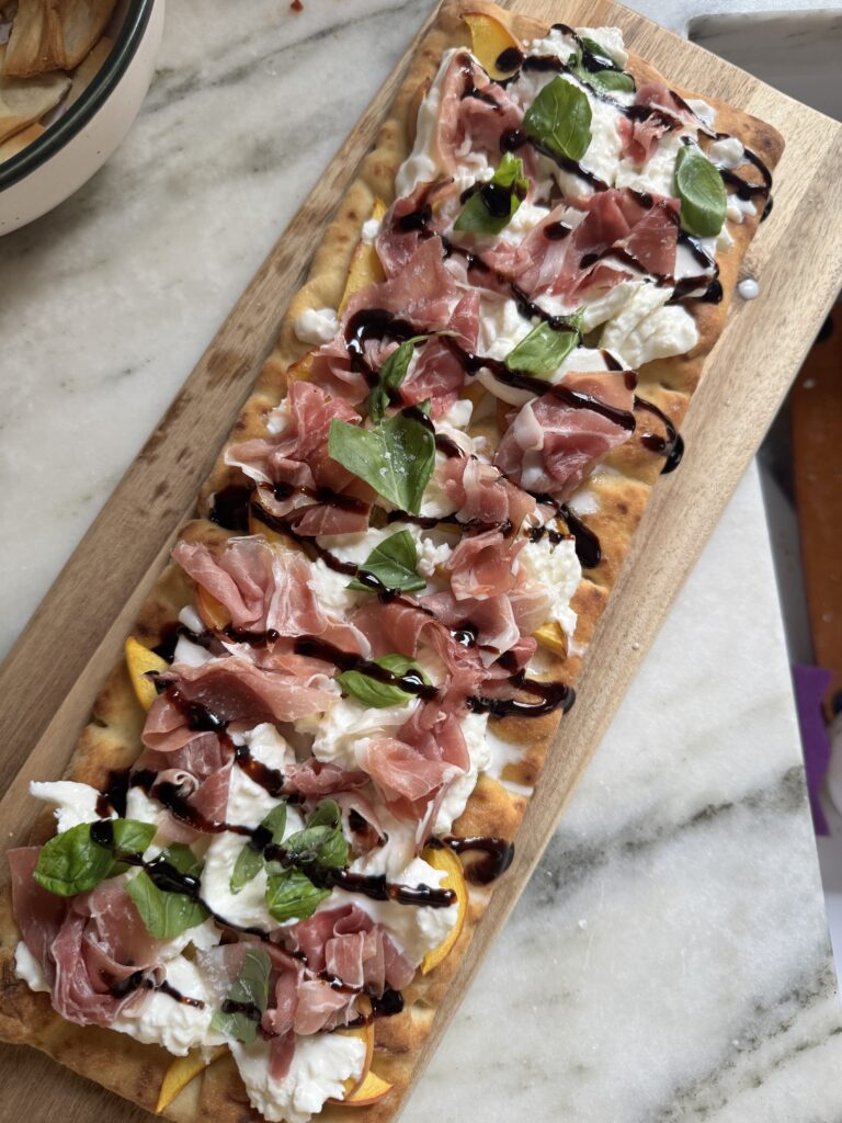 Prosciutto burrata peach flatbread pizza with balsamic glaze on a wooden board