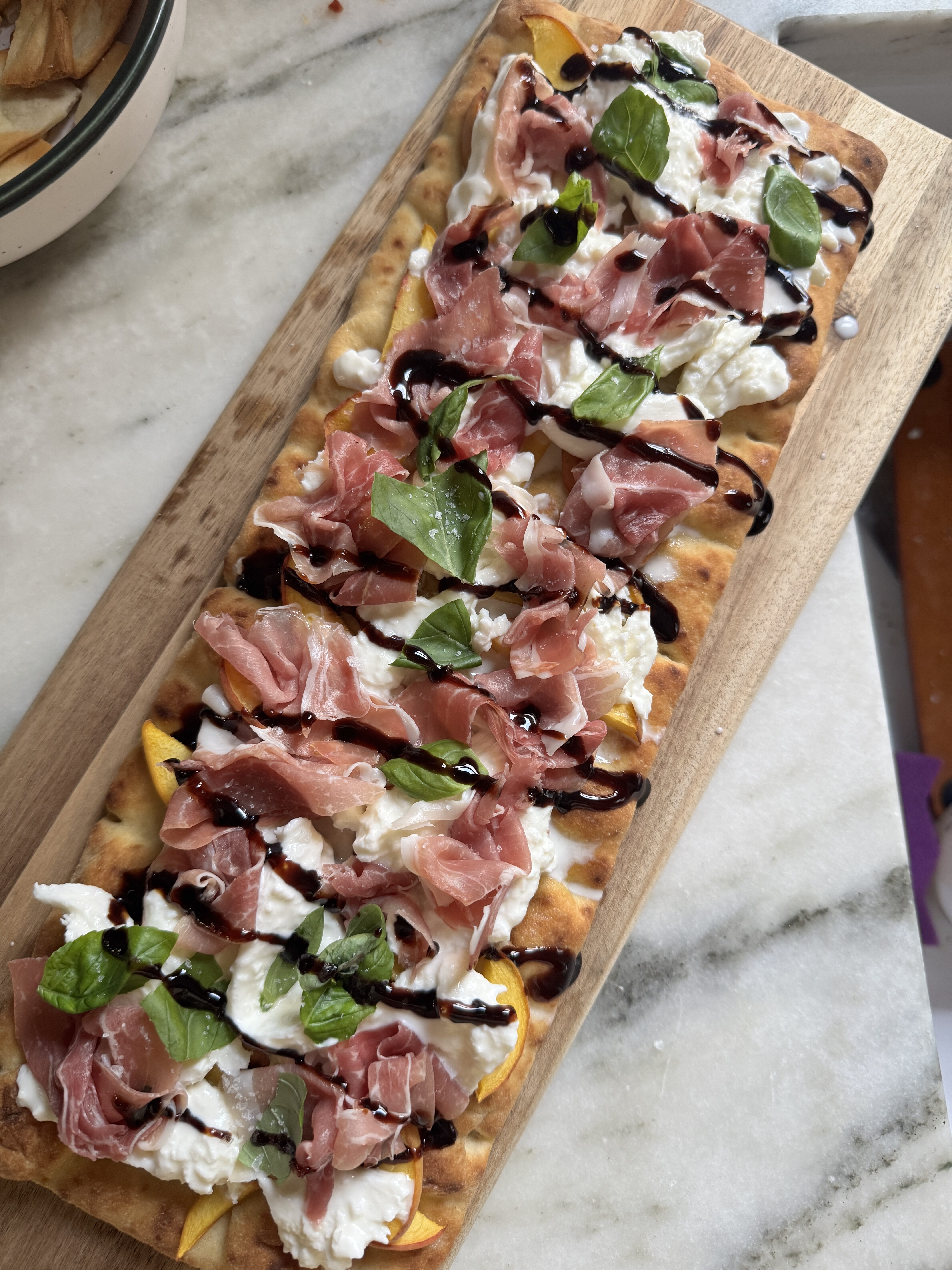 Prosciutto burrata peach flatbread pizza with balsamic glaze on a wooden board