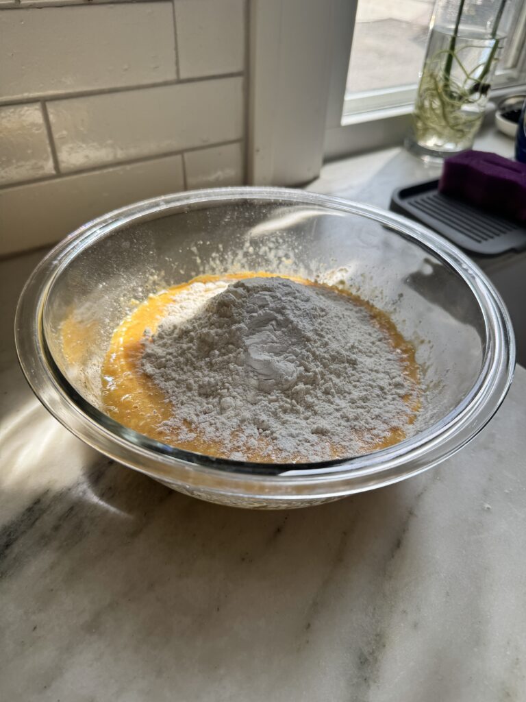 Flour and baking powder added to an egg and cottage cheese batter in a bowl