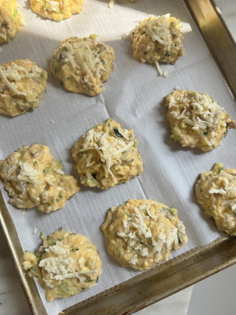 Scoops of zucchini sausage biscuit batter dropped onto a parchment lined baking sheet before baking