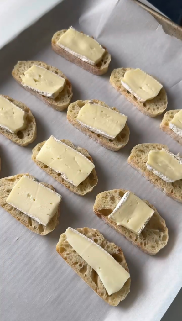 Baguette slices topped with brie on a parchment-lined baking sheet