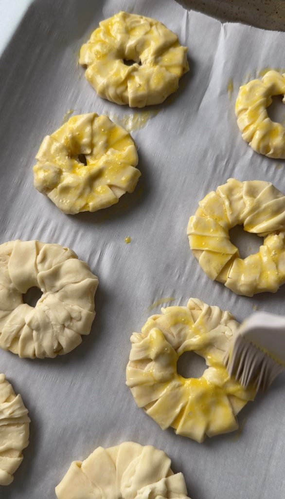 Brushing egg wash over the wrapped apple rings