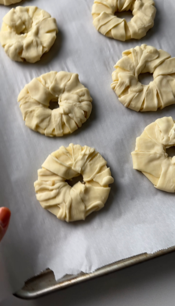 Apple rings wrapped in puff pastry on a baking sheet