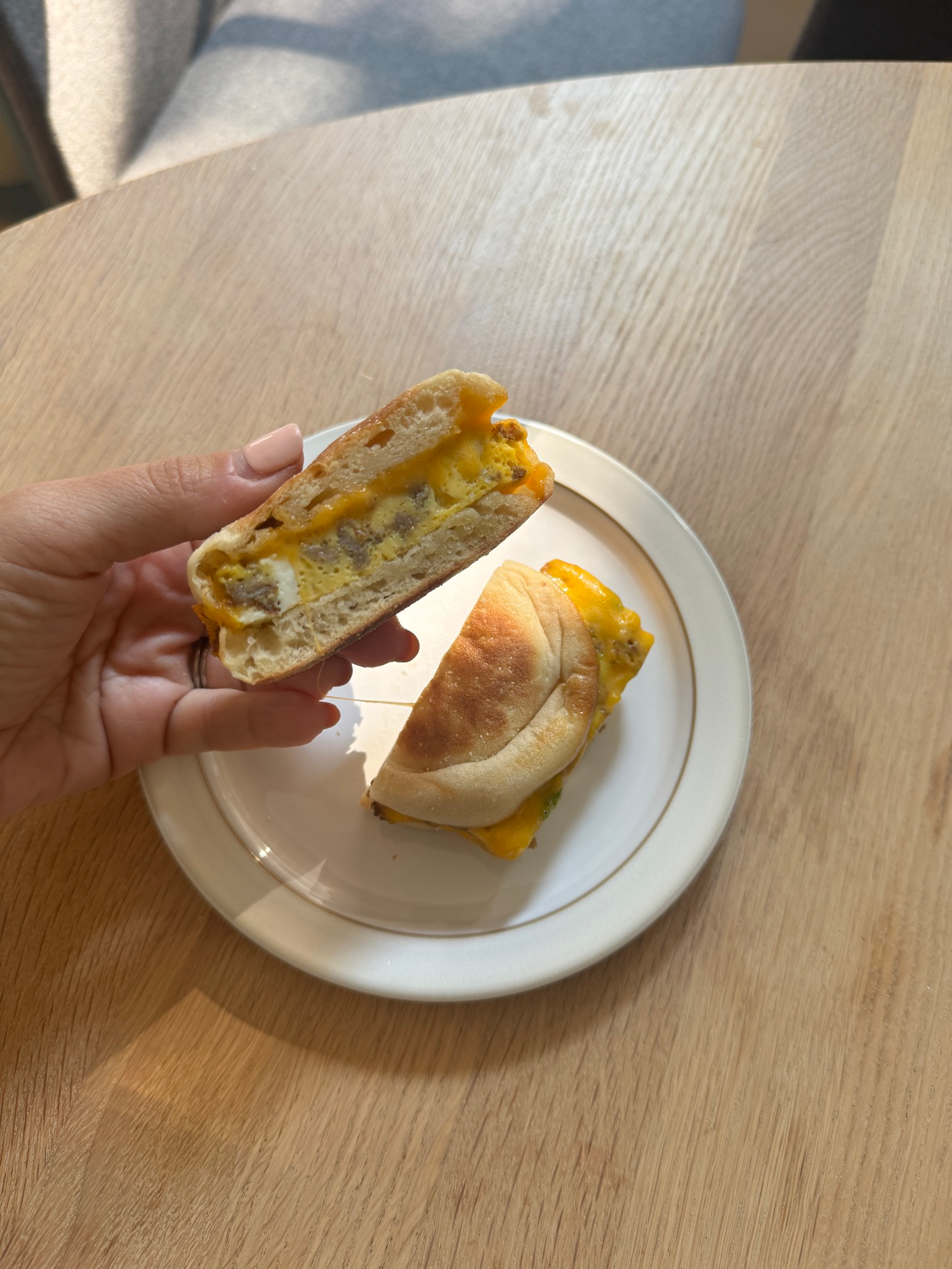 A sausage and scallion breakfast sandwich cut in half showing the egg, sausage, and cheddar