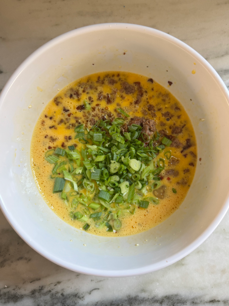 Whisked eggs with cottage cheese, sausage, scallions, and chili flakes in a bowl